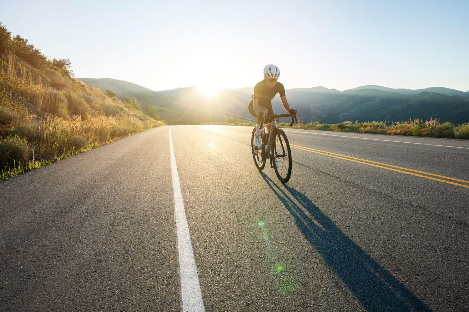 A cyclist in black gear on a TORAYCA® carbon fiber road bike, riding along a winding road outdoors.